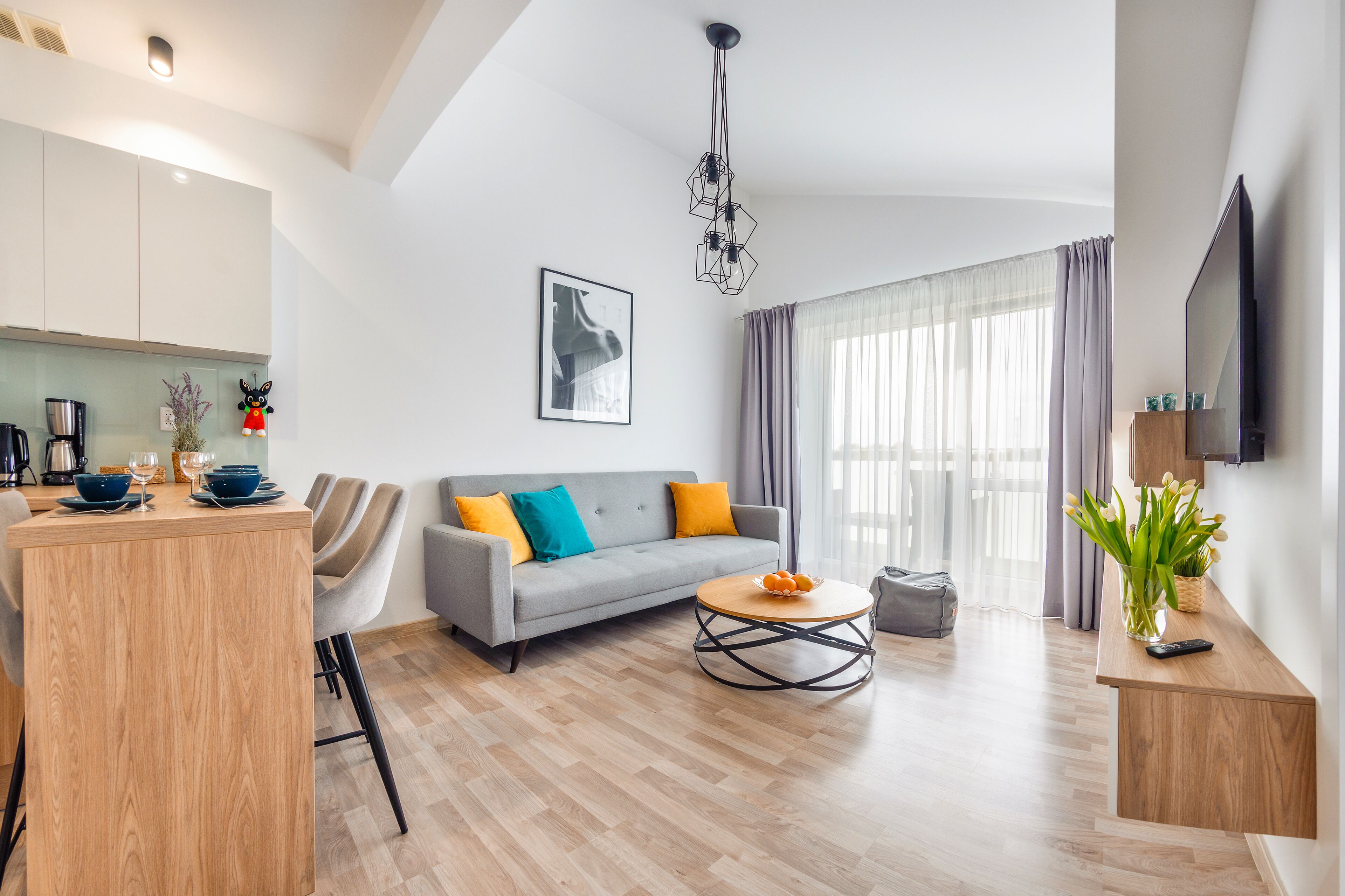 A modern living room with a grey sofa, wooden coffee table, and a kitchen area with a coffee machine.
