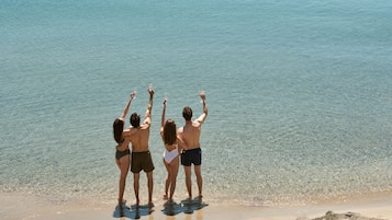 Three people standing at the edge of a beach, facing the water.