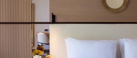 Habitación de hotel con pared de paneles de madera, una mesita redonda con un jarrón de flores, una cama blanca con dos almohadas y un teléfono instalado en la pared.