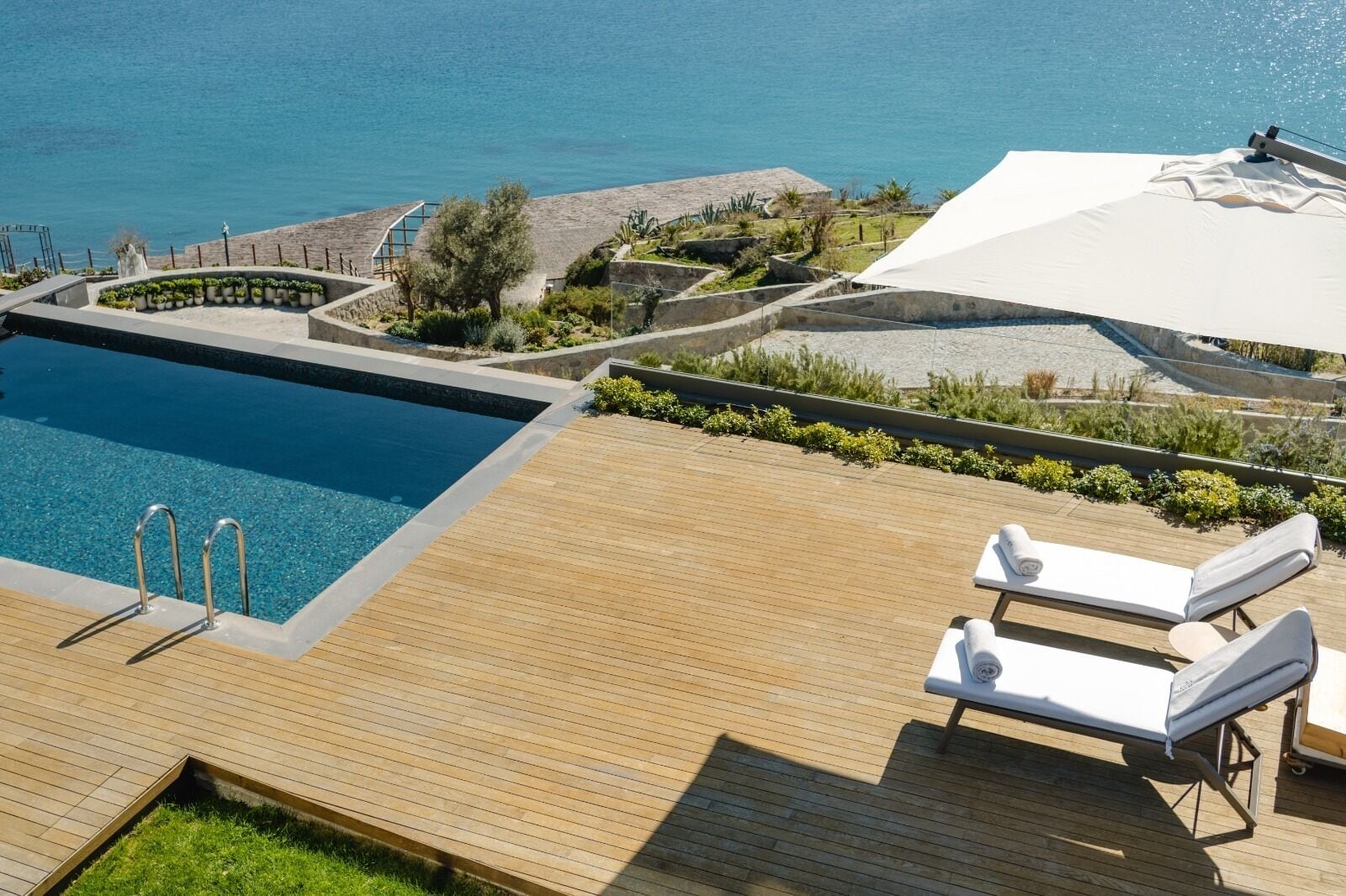 Una piscina con cubierta de madera, sillas de descanso y vista al mar.