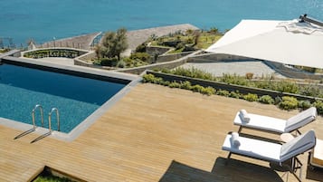 Una piscina con cubierta de madera, sillas de descanso y vista al mar.