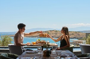 Una pareja cenando en una mesa con vista al mar y las colinas.