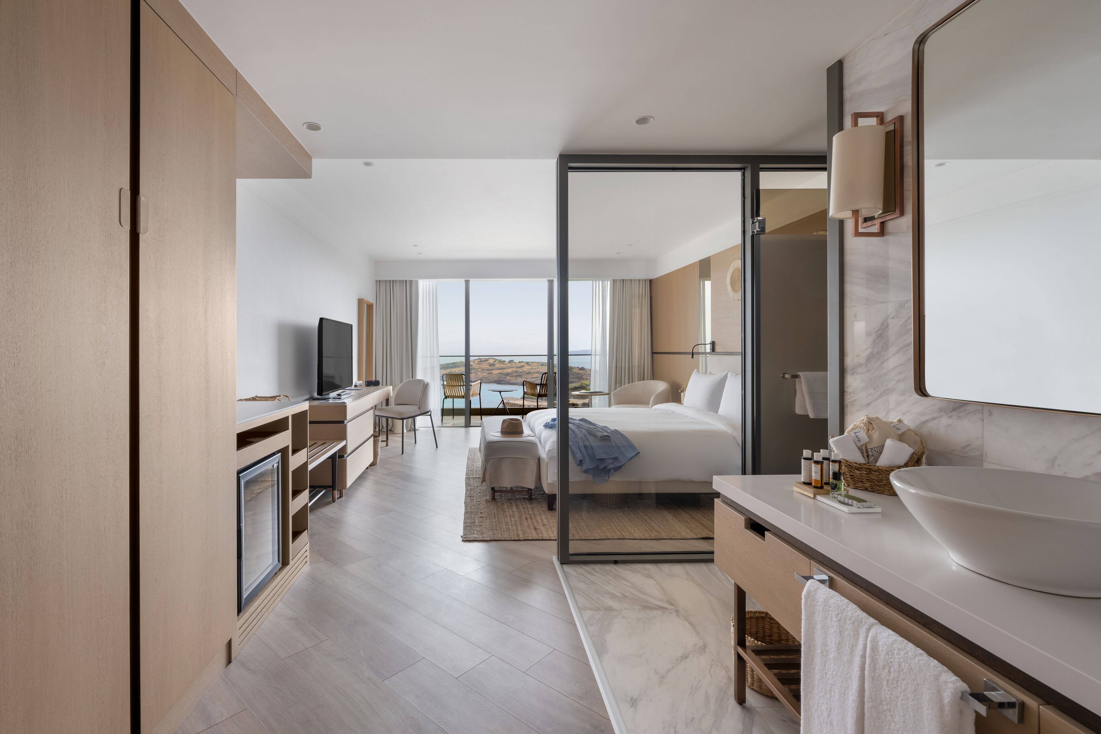 A modern hotel room with a large bed, a bathroom with a large sink, and a view of the outdoors.