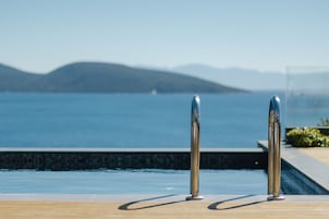 Zona de piscina con barandillas de metal y vistas al mar y montañas a la distancia.