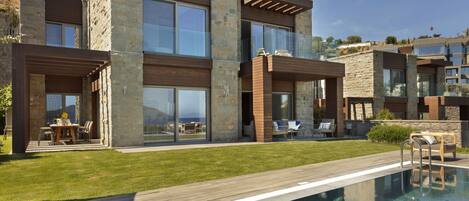 A modern two-story house with a swimming pool, outdoor seating, and a stone facade.