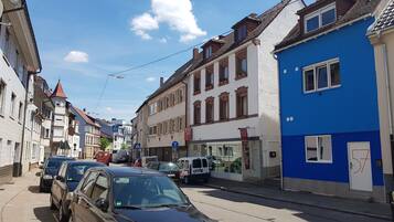 Eine schmale Straße, gesäumt von mehrstöckigen Gebäuden, von denen einige im Erdgeschoss Geschäfte beherbergen.