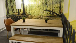 Ein Essbereich mit einem Holztisch und Bänken, einem braunen Ledersessel und einem Wandbild mit Waldmotiv.
