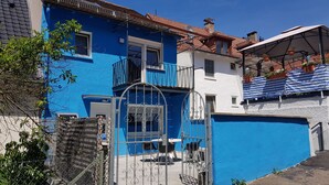 Ein blaues Gebäude mit Balkon, Tor und einer überdachten Veranda mit Blumentöpfen.