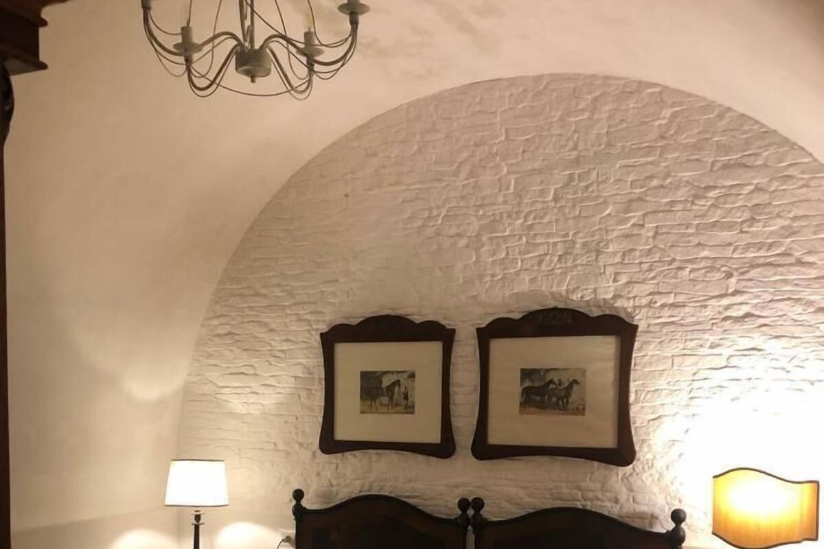 A cozy bedroom with a large bed, two bedside lamps, and a chandelier.