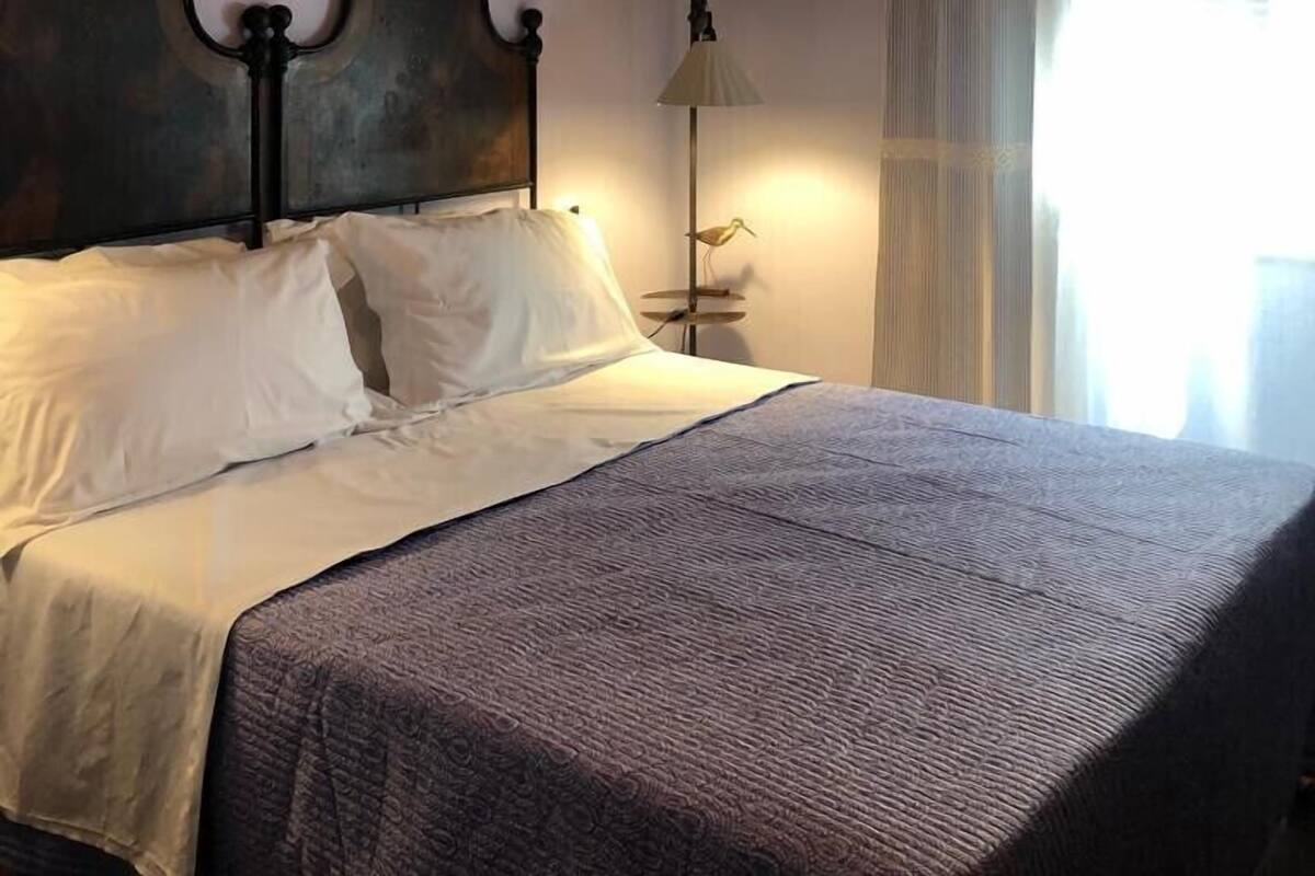 A bedroom with a bed, a headboard with a floral arrangement, a floor lamp, and a window with curtains.