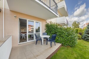 Un balcón con mesa y sillas, un ventanal de vidrio que da a una habitación y un jardín bien cuidado.