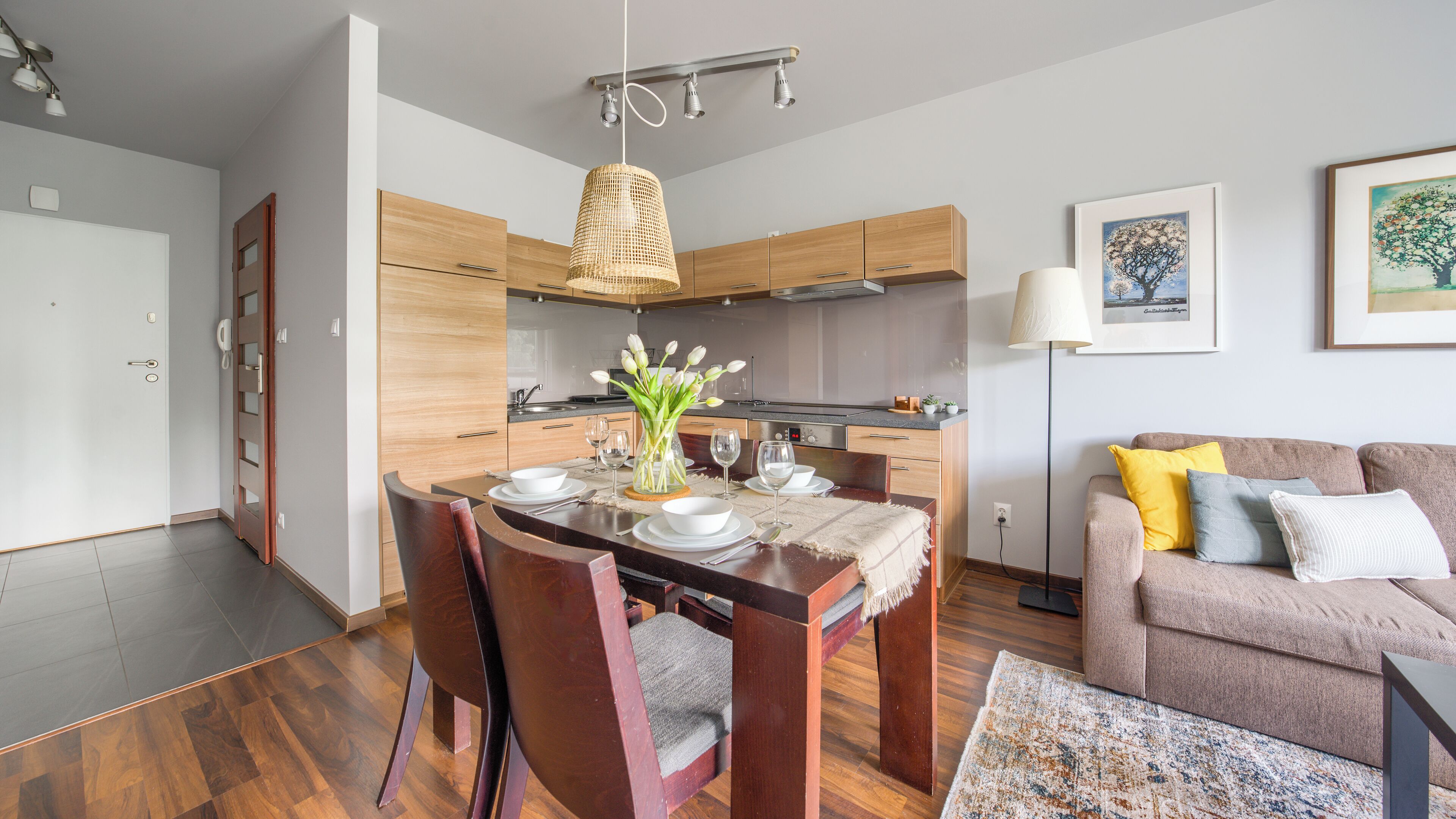 Una cocina moderna con armarios de madera, una mesa de comedor para cuatro personas y una sala de estar con sofá y alfombra.