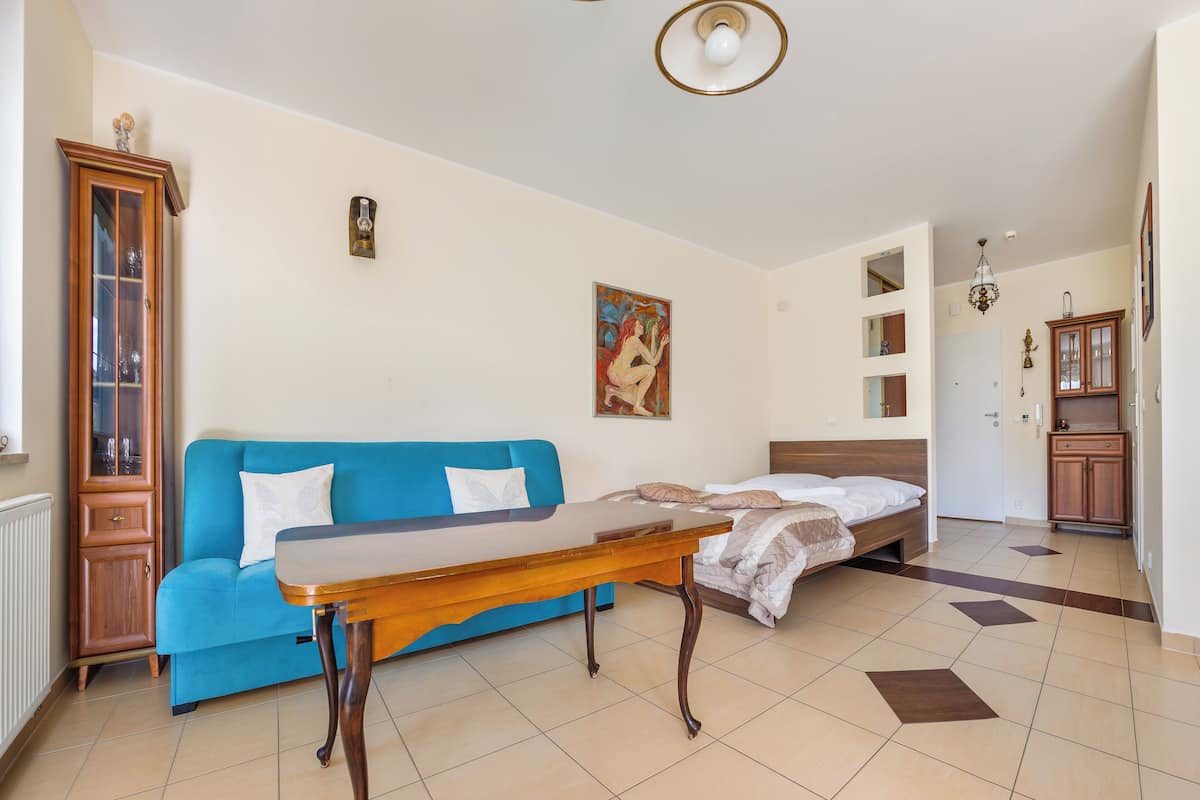 Una habitación con un sofá azul, una mesa de madera, una cama con cabecera blanca y un armario de madera.