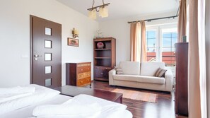A hotel room with a bed, a sofa, a wooden dresser, a bookshelf, and a window with curtains. - Sun & Snow Bałtyk Park (Kolobrzeg)