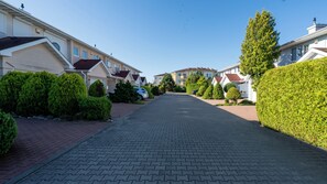 A residential street lined with houses, paved with interlocking bricks, and surrounded by well-maintained hedges and trees. - Sun & Snow Bałtyk Park (Kolobrzeg)