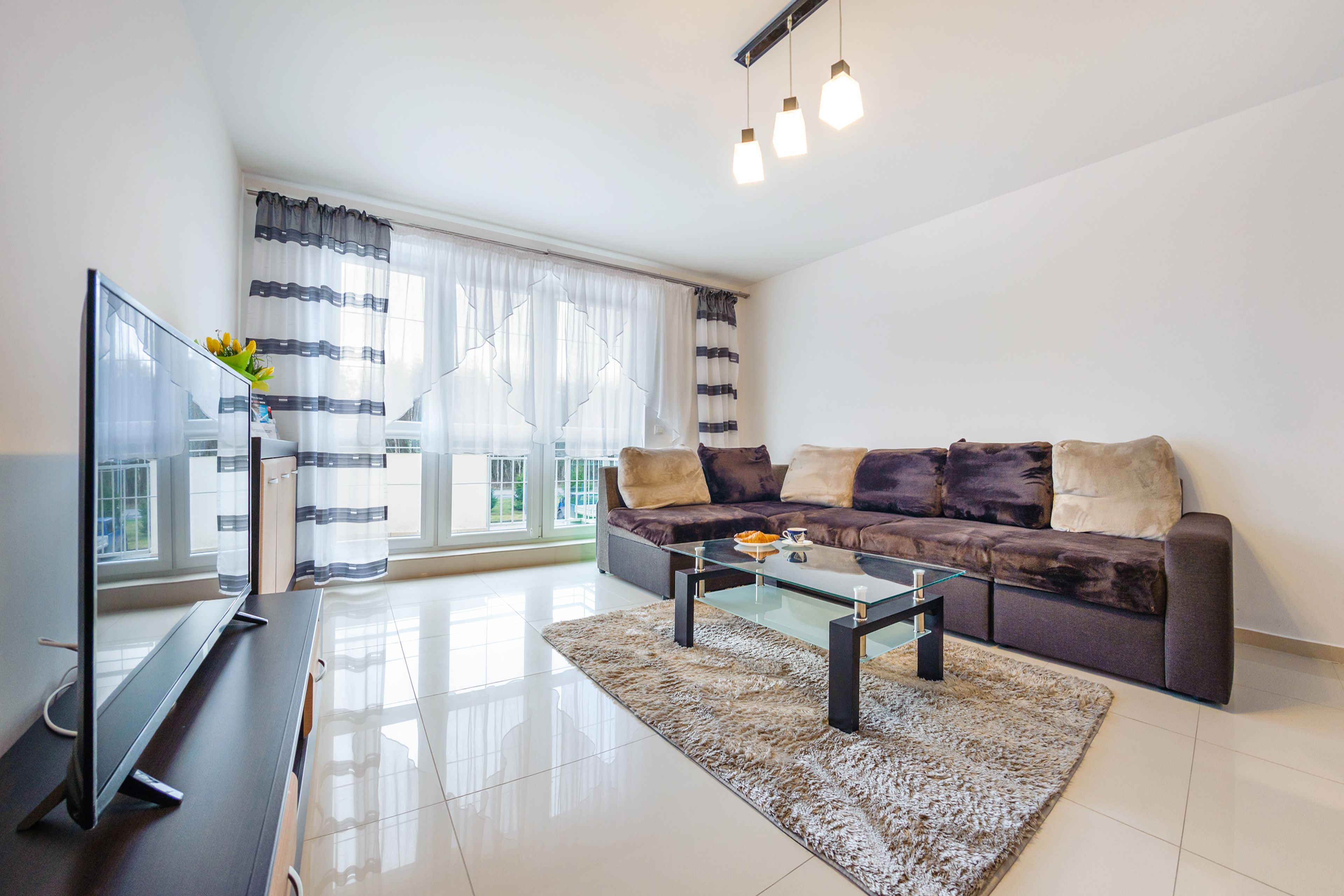 Una sala de estar moderna con un televisor de pantalla plana, una mesa de centro de vidrio y un sofá con cojines.