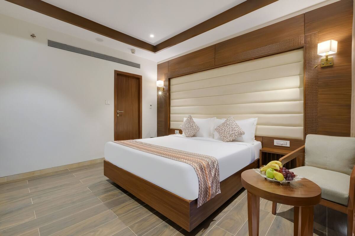A hotel room with a large bed, a wooden headboard, a small table with fruit, and a chair.