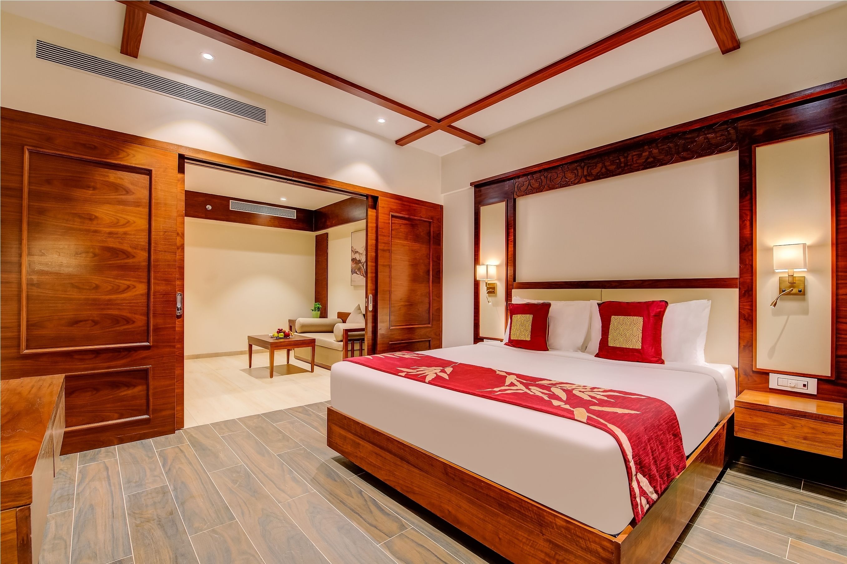 A spacious bedroom with a large bed, wooden wardrobe, and a small seating area.