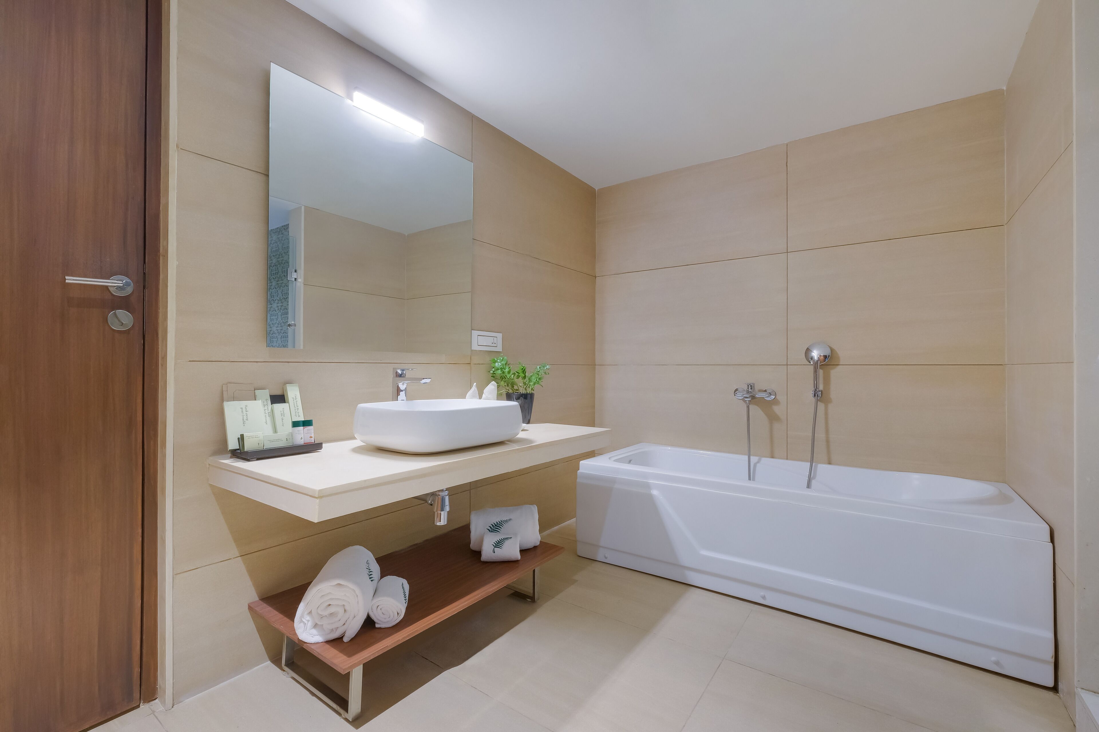 A modern bathroom with a large bathtub, a sink with a mirror above it, and a shelf with towels.