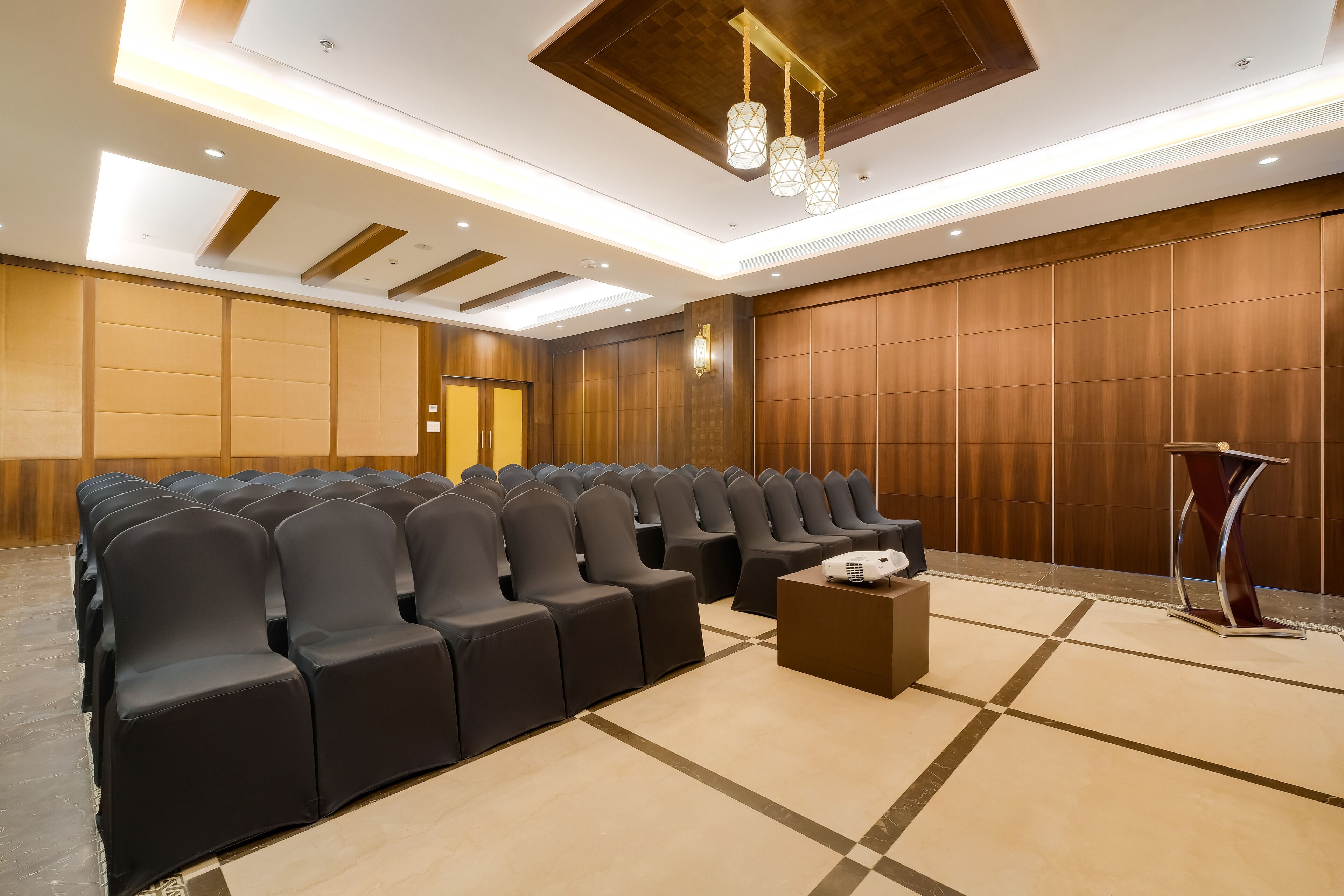 A conference room with rows of black chairs, a podium, and a projector on a table.