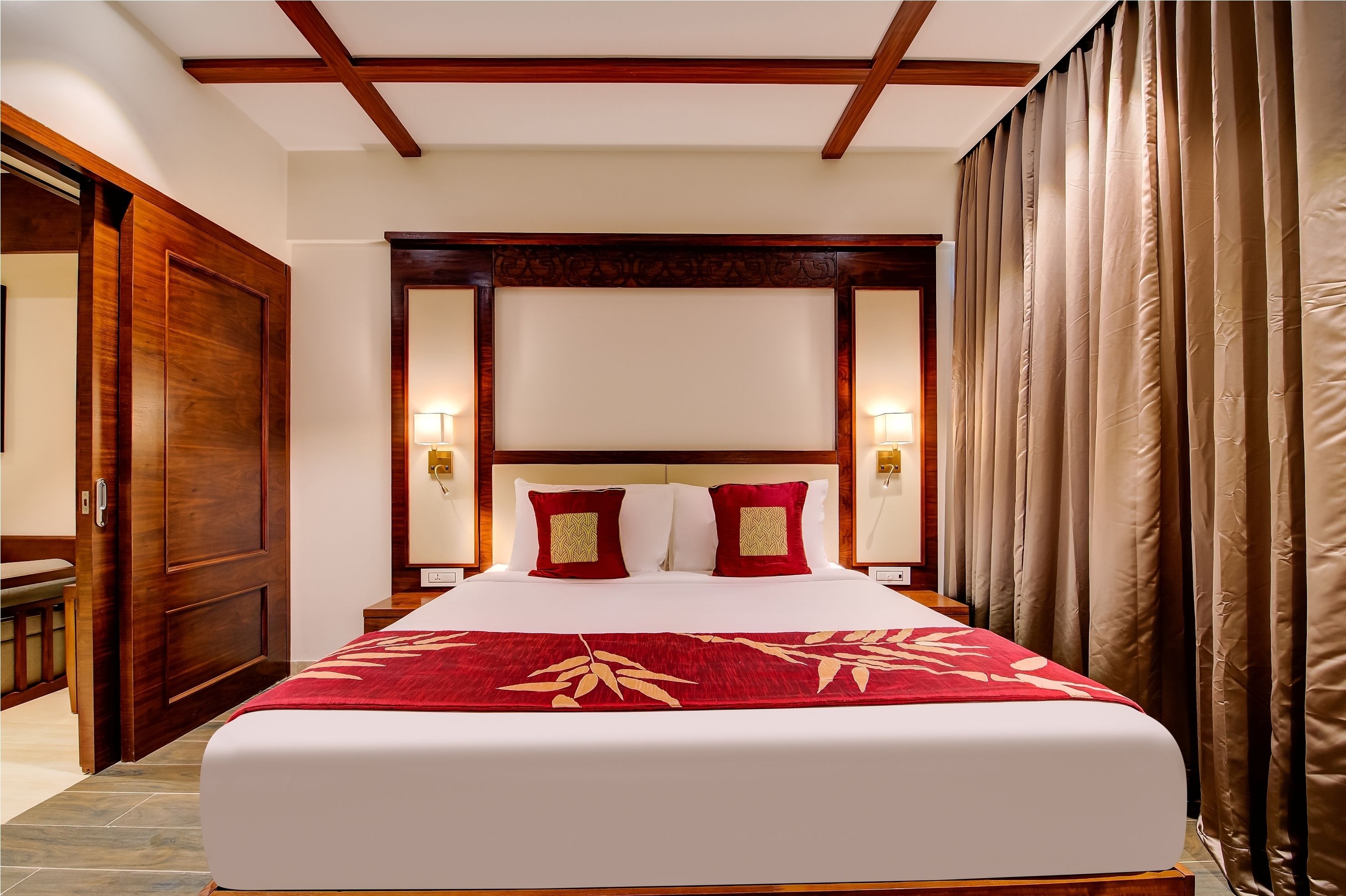 Une chambre d’hôtel avec un grand lit, une tête de lit en bois et une couvre-lit rouge.