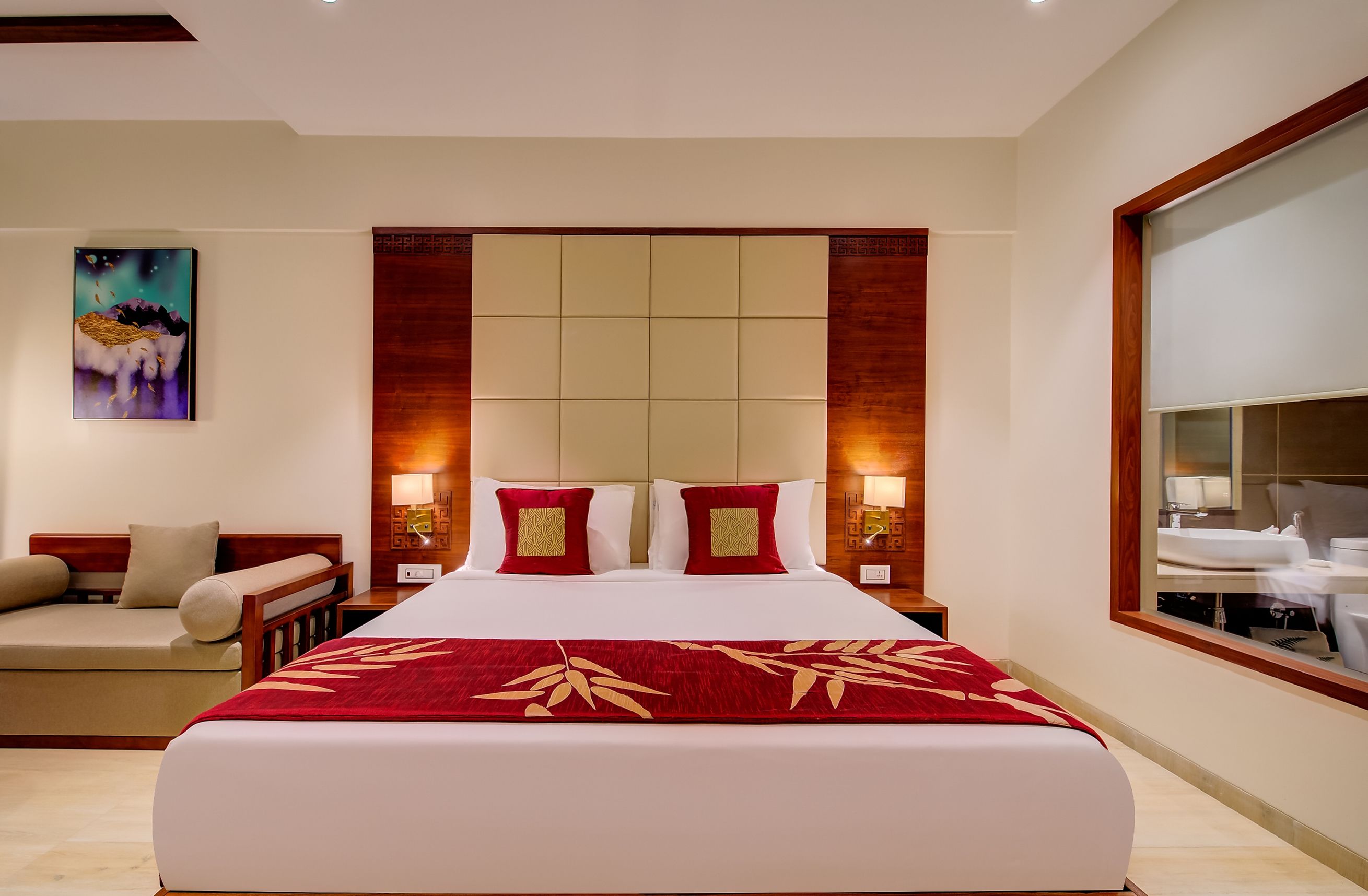 A hotel room with a large bed, a sofa, a nightstand with a lamp, and a large mirror.