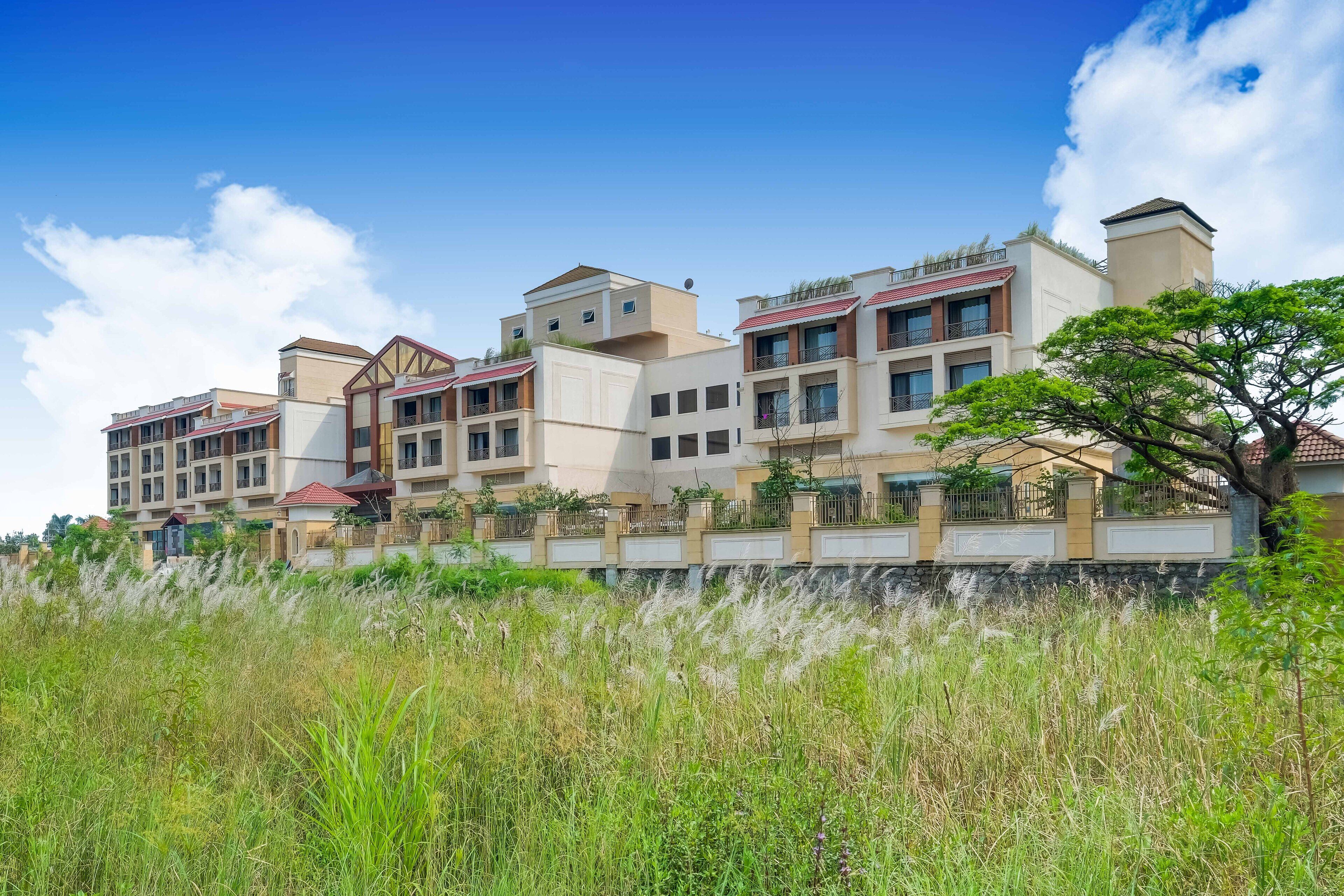 A multi-story residential building with a modern architectural style, featuring balconies and a landscaped front yard.
