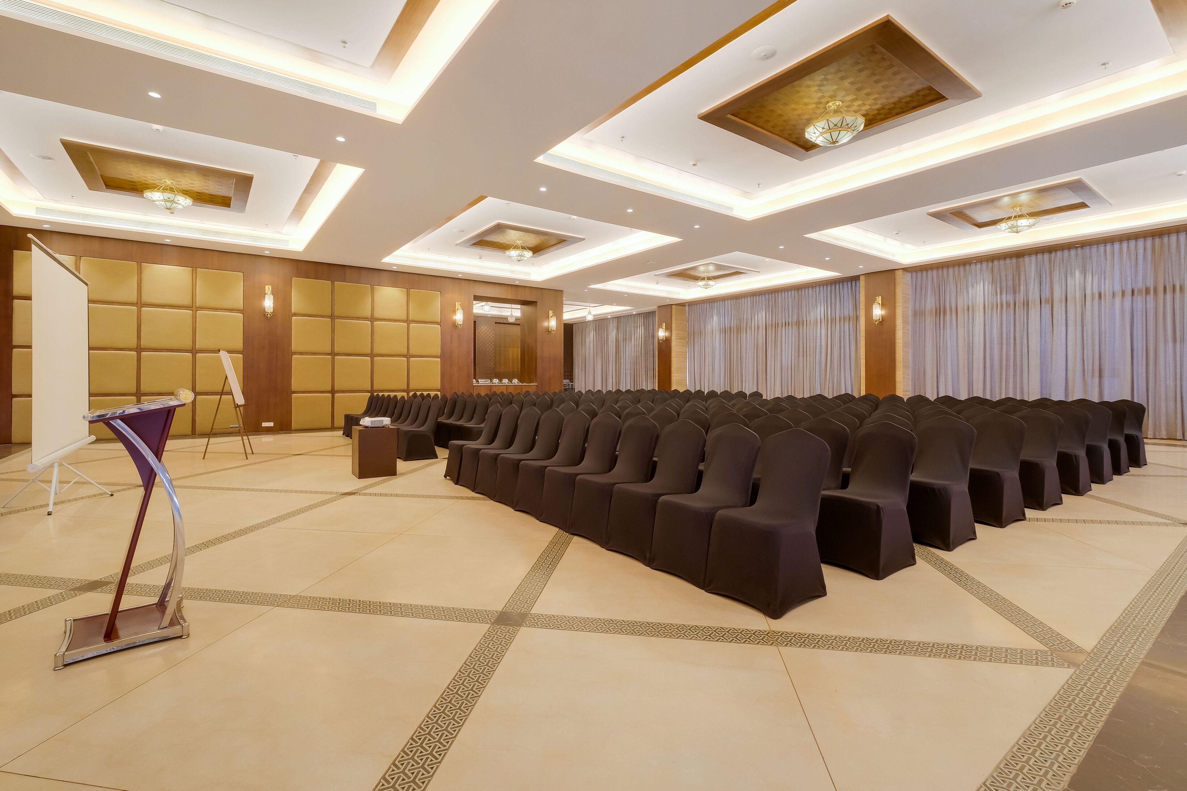 A conference room with rows of black chairs, a podium, and a large screen.