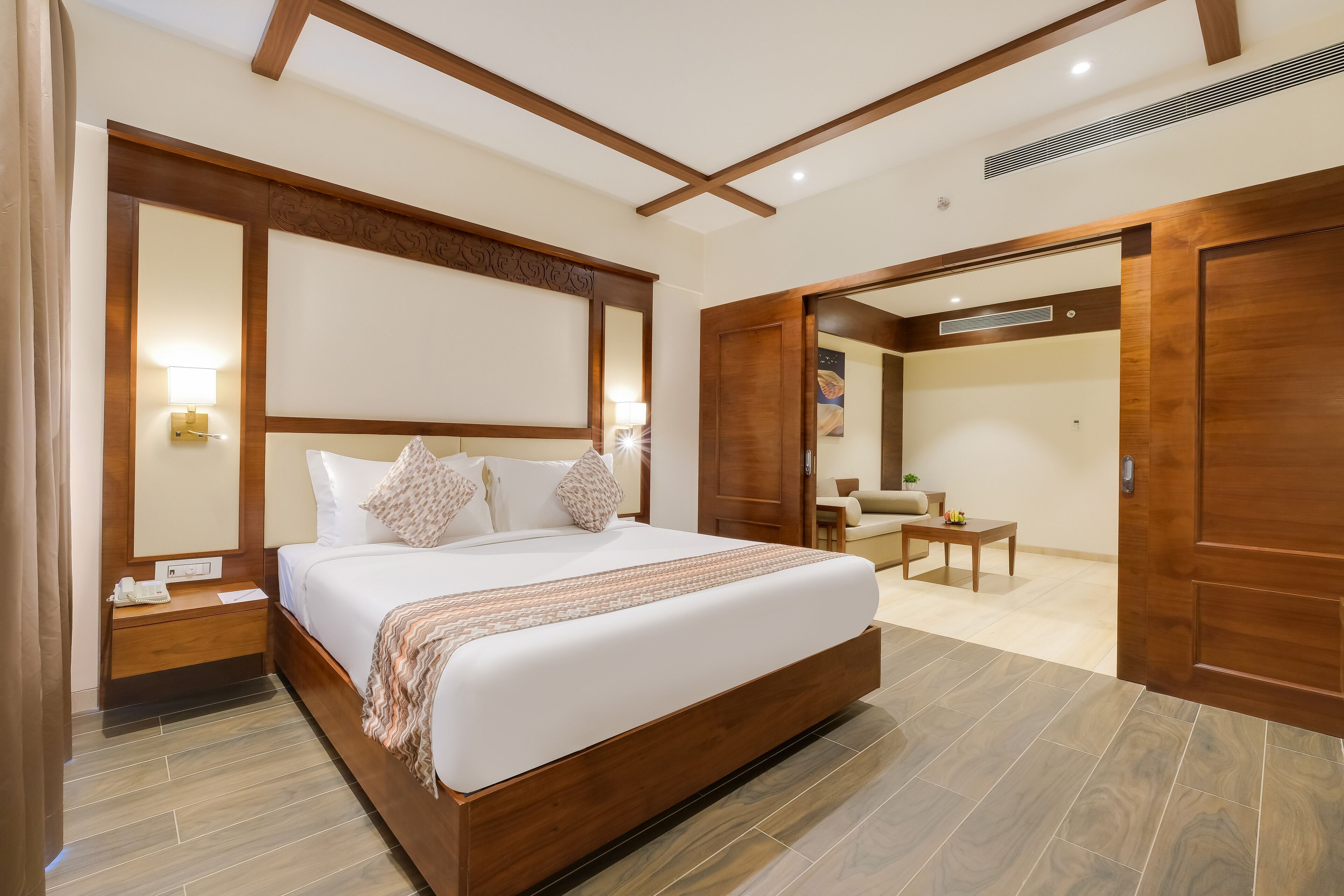 A modern hotel room with a large bed, wooden headboard, bedside tables, a desk, and a chair.