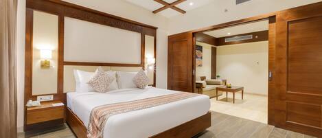 A modern hotel room with a large bed, wooden headboard, bedside tables, a desk, and a chair.