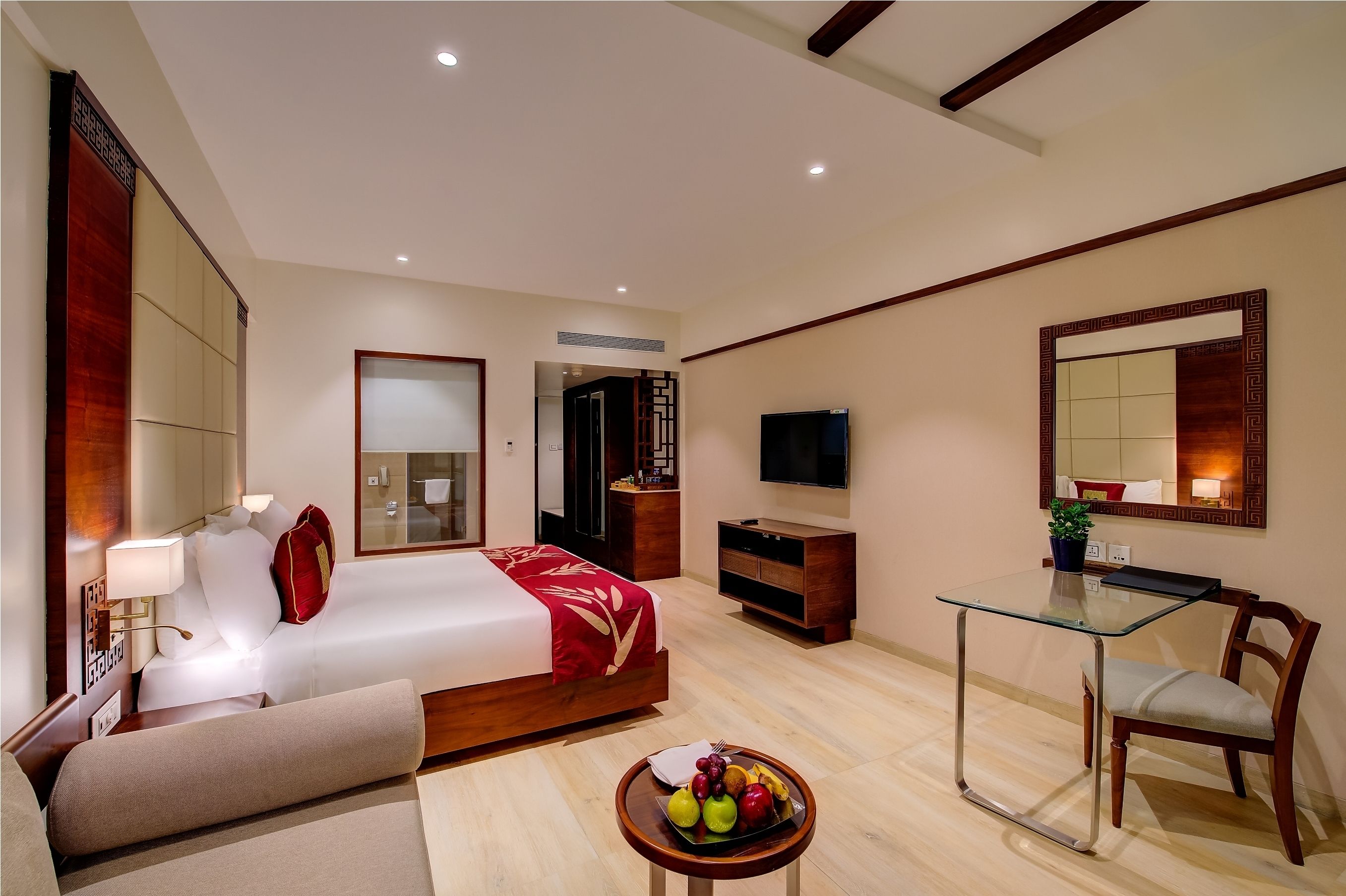 Habitación de hotel moderna con cama, mesita de noche, televisor, escritorio, silla y una pequeña mesa con fruta.