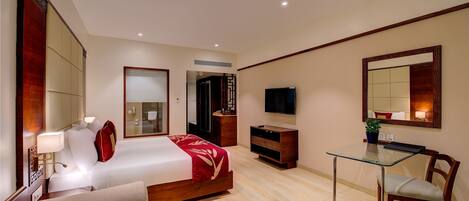 Habitación de hotel moderna con cama, mesita de noche, televisor, escritorio, silla y una pequeña mesa con fruta.