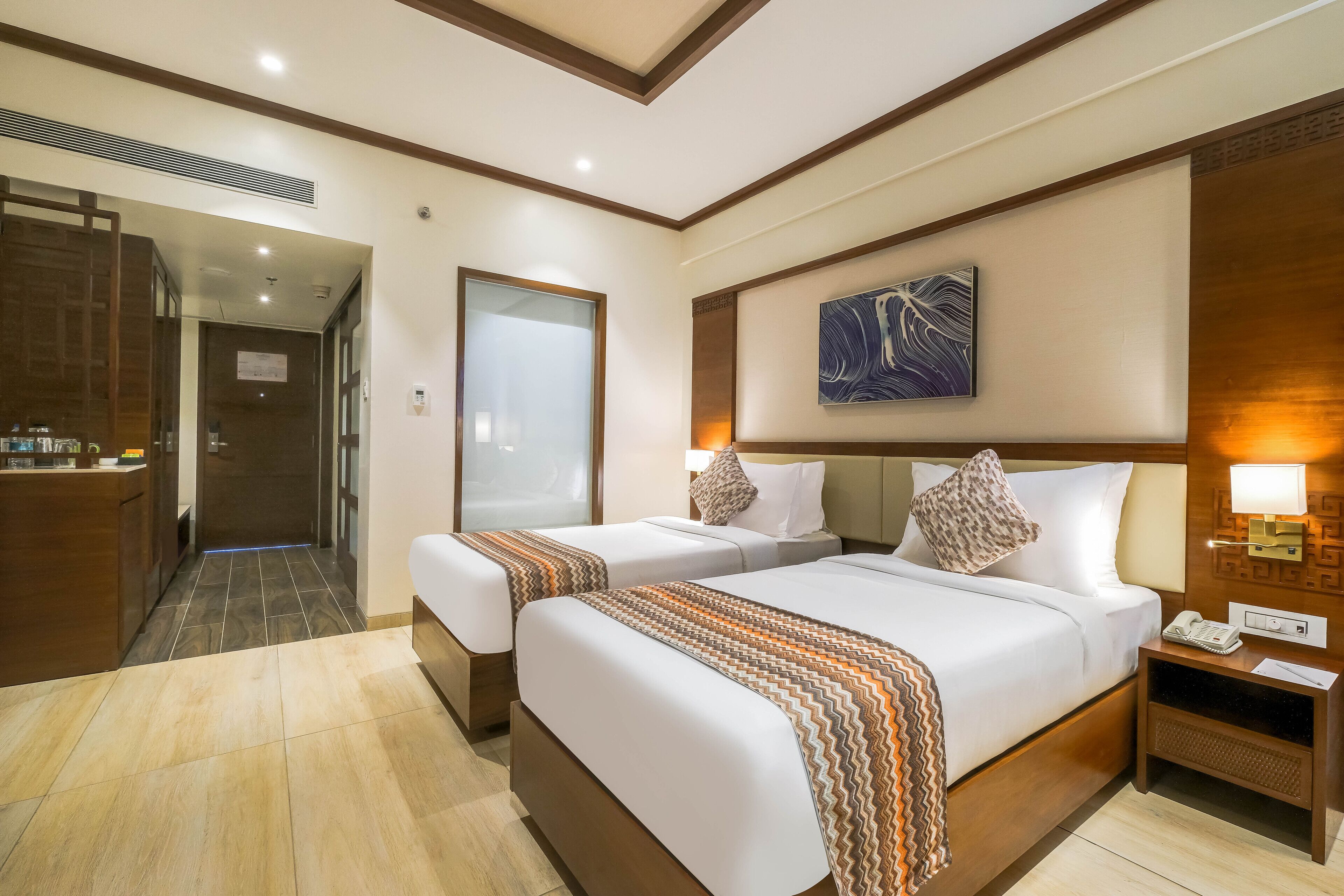 A hotel room with two beds, a desk, and a bathroom.