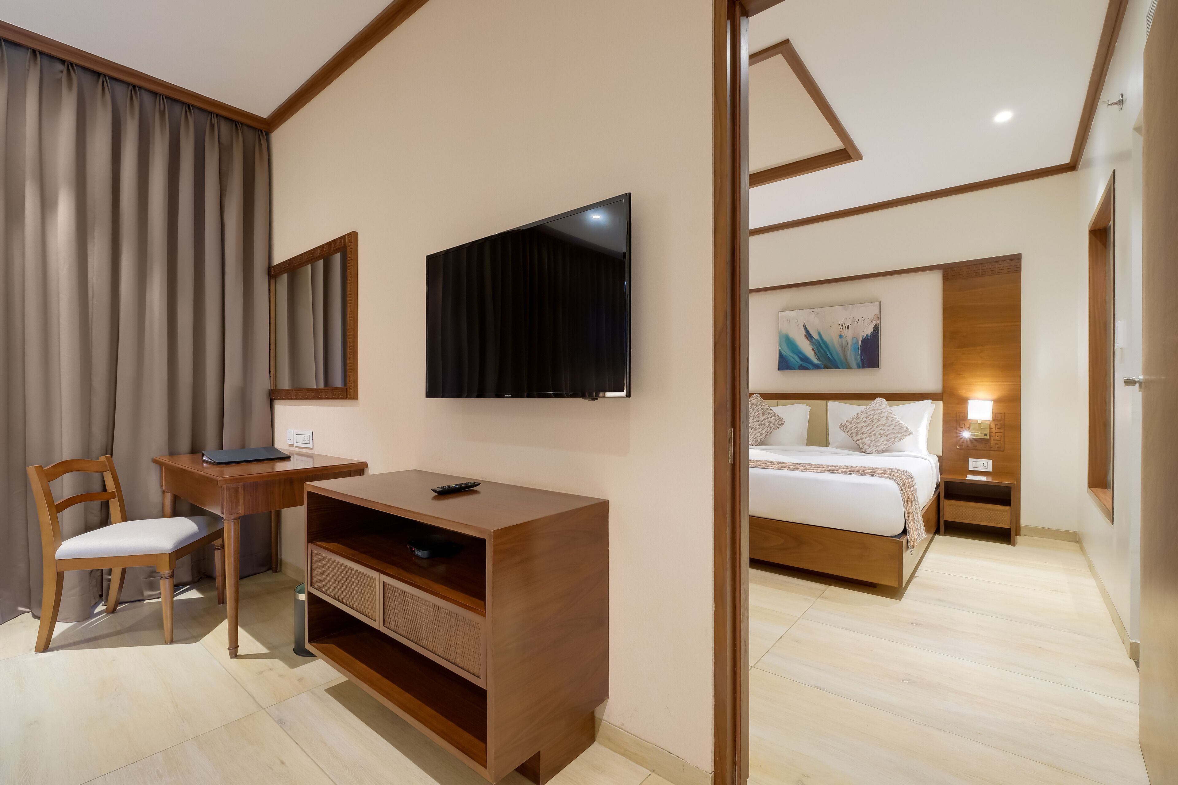 Een moderne hotelkamer met een houten bureau, stoel, flatscreen televisie en een bed met hoofdeinde.
