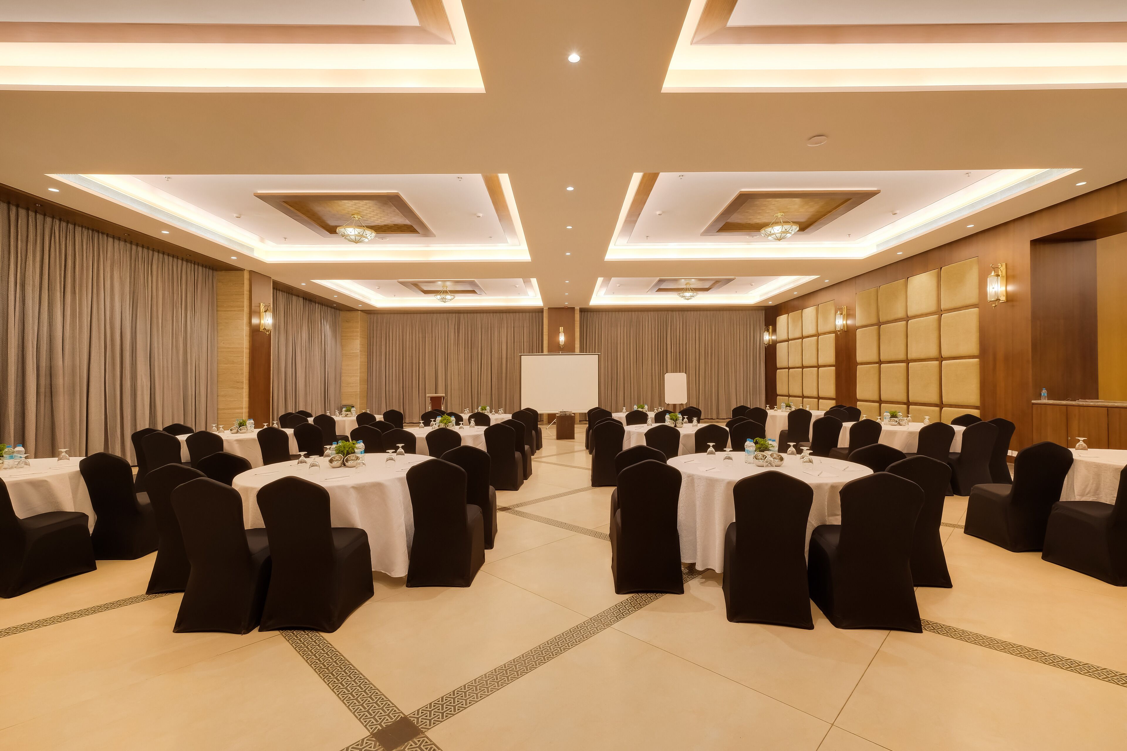 A conference room with multiple round tables, black chairs, and a whiteboard at the front.