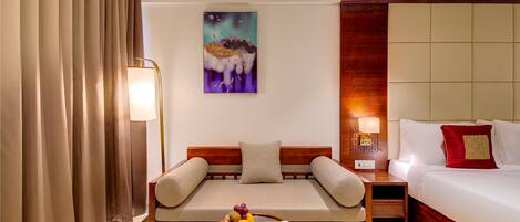 Habitación de hotel con sofá, una mesa de comedor con fruta, cama y un cuadro en la pared.