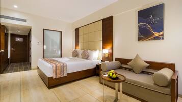 A hotel room with a large bed, a sofa, a small table with fruit, and a painting on the wall.
