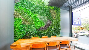A wooden table with four chairs, a green leafy wall, and a sign with "AXA" on it. - Life Style Surabaya (Surabaya)