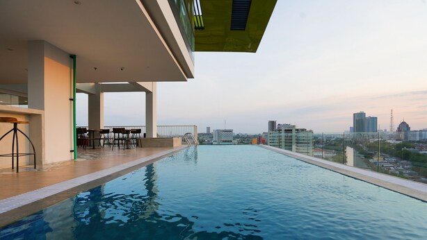 A modern indoor swimming pool with a city view, surrounded by a covered area with seating. - Life Style Surabaya (Surabaya)