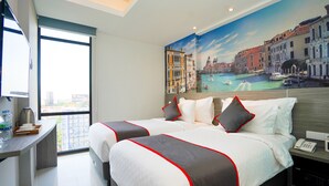 A hotel room with two beds, a desk with a water bottle, and a mural of Venice. - Life Style Surabaya (Surabaya)