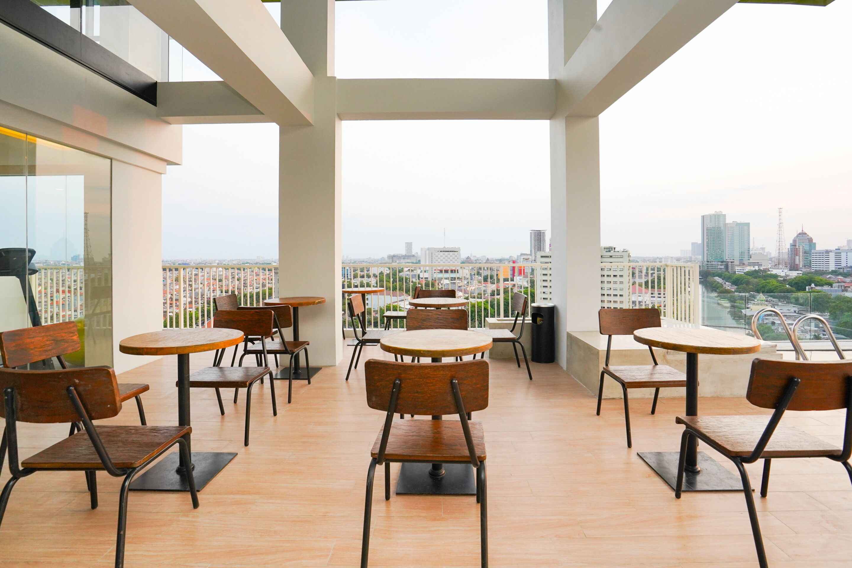 Ein geräumiger Balkon mit mehreren Holztischen und Stühlen und Blick auf die Stadt.