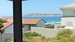 A coastal view with a building and a house in the foreground, a clear sky, and the sea in the background. - Betty (Plettenberg Bay)