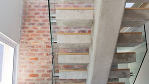 A modern staircase with glass railings, concrete steps, and a brick wall. - Betty (Plettenberg Bay)