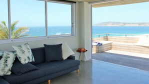 A modern living room with a large window overlooking a coastal view. - Betty (Plettenberg Bay)