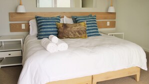 A neatly made bed with white bedding and decorative pillows, a wooden headboard, and bedside tables with lamps. - Betty (Plettenberg Bay)