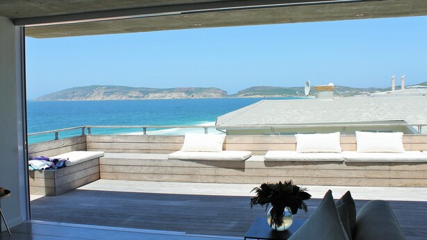 A modern outdoor seating area with a view of the ocean and hills. - Betty (Plettenberg Bay)