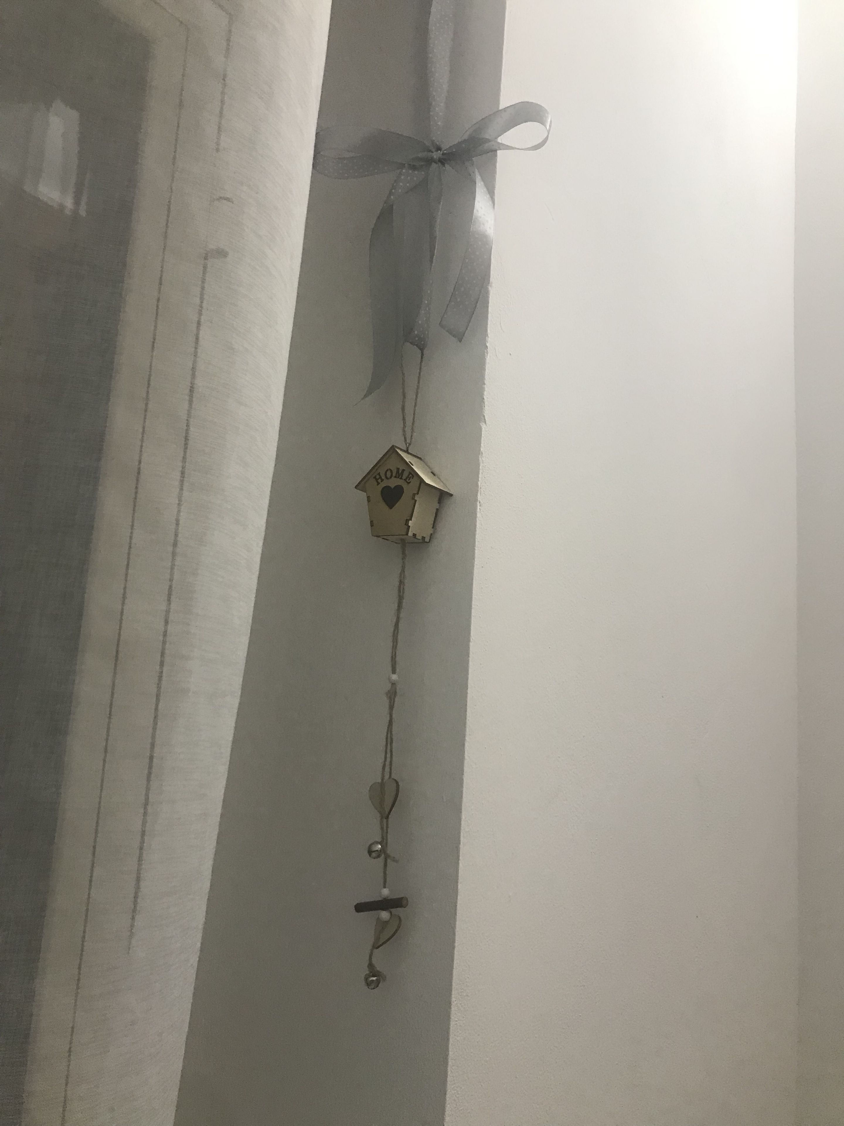 A wall-mounted decoration with a house-shaped ornament, a ribbon, and a string with heart-shaped charms.
