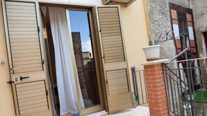 A residential building with a sliding glass door, a small balcony with a potted plant, and a metal gate. - B&b Il Cortile (Mazzarino)