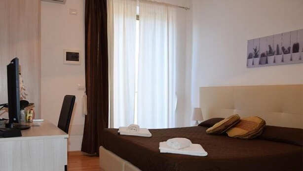 A hotel room with a bed, a desk, a chair, a TV, and a window with curtains. - B&b Il Cortile (Mazzarino)