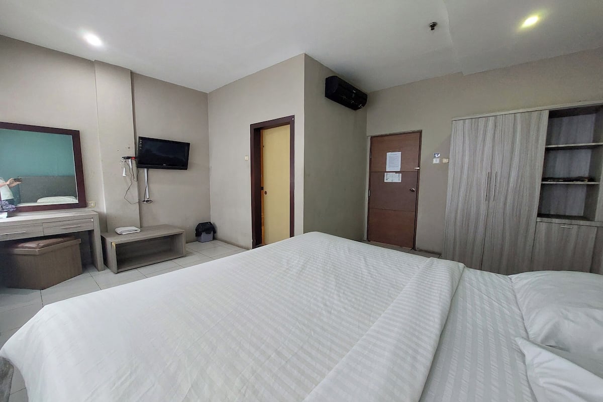 A hotel room with a large bed, a TV mounted on the wall, a wardrobe, and a desk with a telephone.